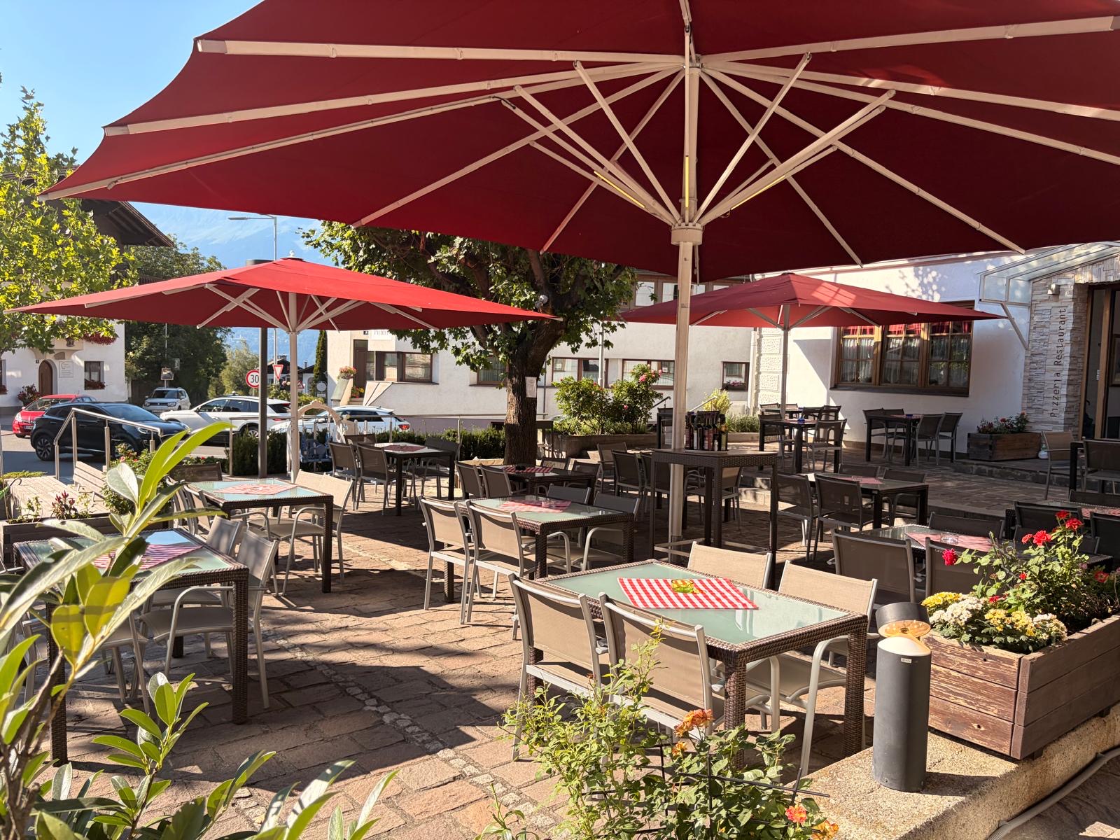 Gastgarten der Pizzeria Giardino mit roten Sonnenschirmen und Blick ins Inntal